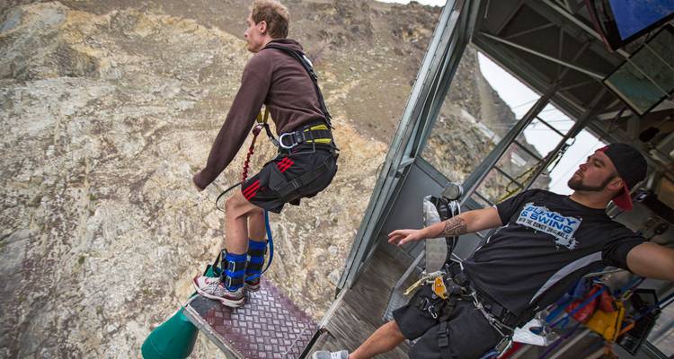 Un participant se penche depuis une plateforme élevée pour un saut à l'élastique tandis qu'un instructeur fournit des conseils.