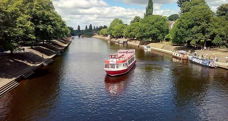 Río con barcos y bordeado de árboles bajo un cielo azul.