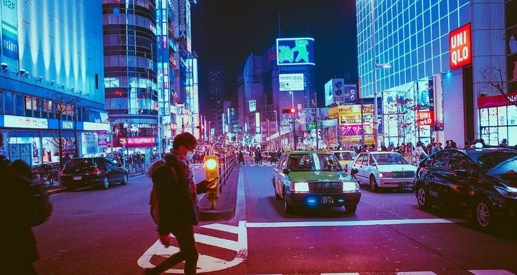 Belebte Stadtstraße bei Nacht mit hellen Neonlichtern.
