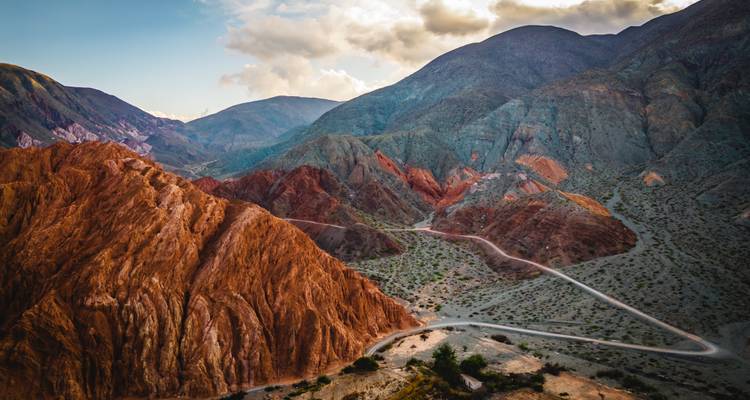 Montañas vibrantes de múltiples colores y sinuosos caminos de tierra en las tierras altas andinas al atardecer.