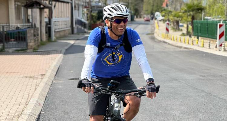 Fietser in blauw shirt glimlacht terwijl hij door een rustige straat in een woonwijk rijdt.