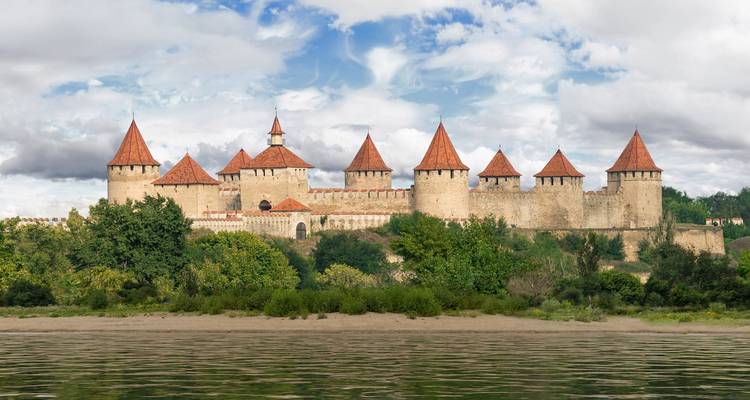 Large stone fortress with multiple towers by a river.
