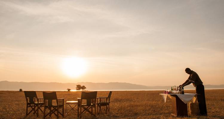 Buiteneetopstelling met stoelen en een tafel bij zonsondergang in een grasveld.