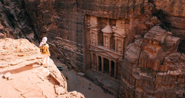 Una persona parada en la cima de un acantilado con vista a la antigua ciudad de Petra.