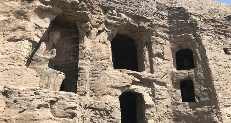 Falaise rocheuse avec niches sculptées et statues anciennes.