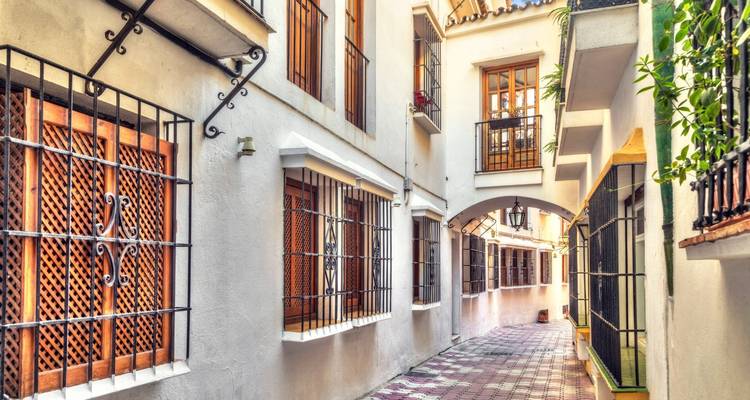 Charmante smalle doorgang met gesmede ijzeren raamroosters en een tegelvloer met patroon in een Andalusisch stadje.