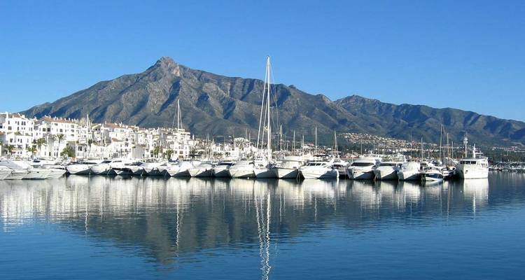 Luxe jachten afgemeerd in een fonkelende jachthaven met een rotsachtig berglandschap op de achtergrond onder helder Andalusisch luchtruim.