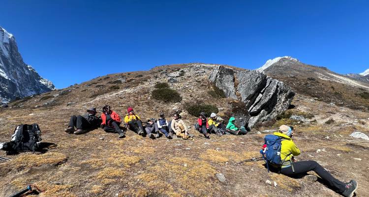 Grupo de excursionistas sentados en una ladera de montaña con cielos despejados.