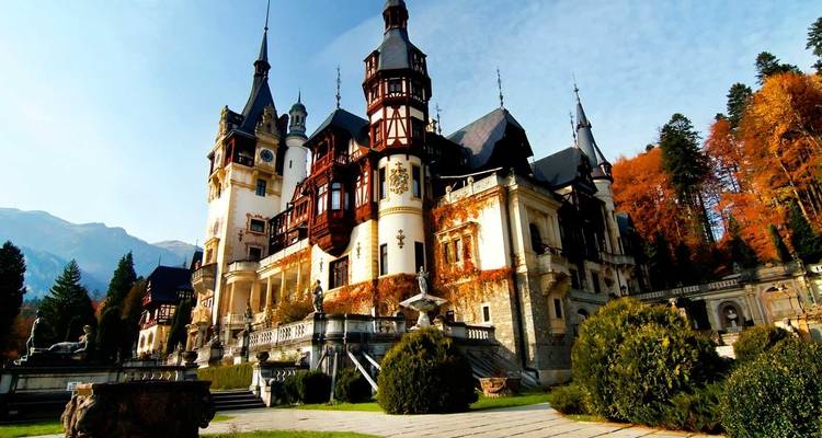 Ornamentado Castillo de Peles rodeado de árboles otoñales con telón de fondo montañoso en Sinaia.