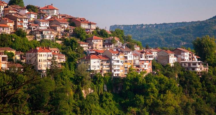 Grupo de casas de tejados rojos que descienden en cascada por una ladera frondosa en Veliko Tarnovo.