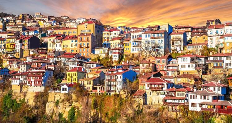 Gouden zonsondergang schildert de gelaagde huizen tegen de rotswand van Veliko Tarnovo in warm licht
