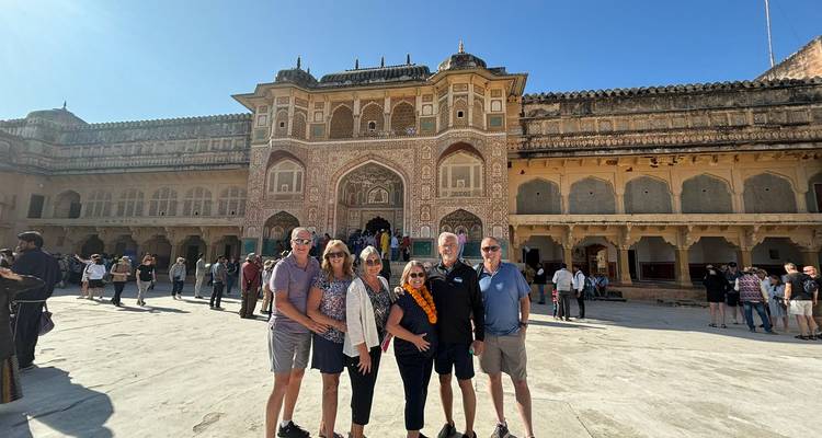 El grupo de turismo se encuentra en el amplio patio frente a la fachada ornamentada del Fuerte Ámbar de Jaipur bajo un cielo azul despejado.