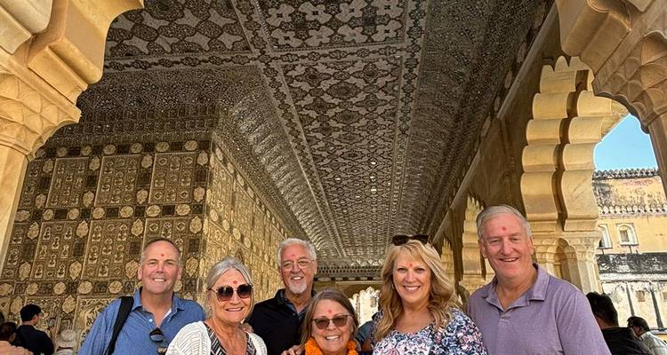 Los visitantes sonríen bajo un techo de espejo con un patrón intrincado dentro del palacio del Fuerte Ámbar de Jaipur.