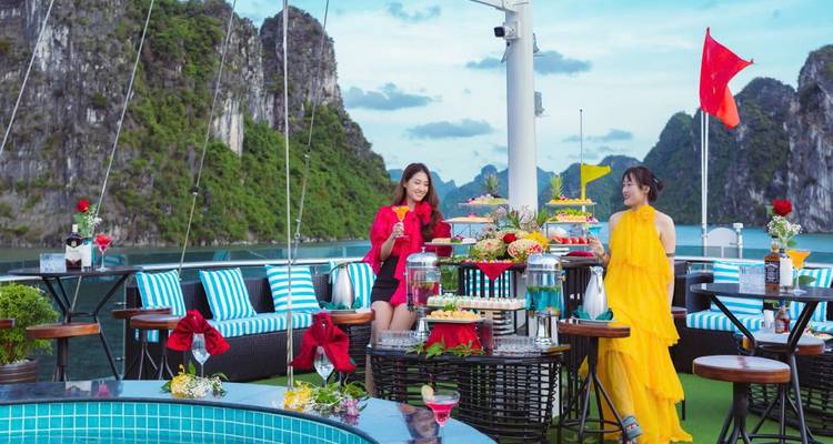 Twee mensen genieten van een maaltijd en drankjes op het dek van een cruise met uitzicht op Halong Bay.