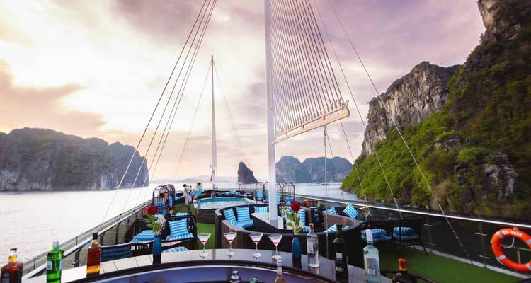 Een stijlvol cruisedek met uitzicht op Halong Bay bij zonsondergang, met drankjes en zitplaatsen.