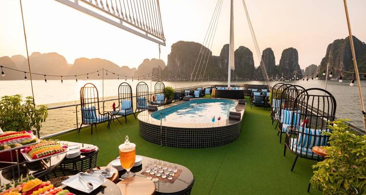 Dek van een luxe cruiseschip bij zonsondergang met een zwembad en loungegebied te midden van Halong Bay.