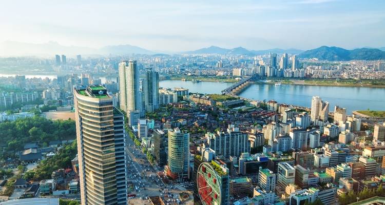 Vue aérienne panoramique de Séoul avec la rivière Han, les ponts et les montagnes lointaines au crépuscule.