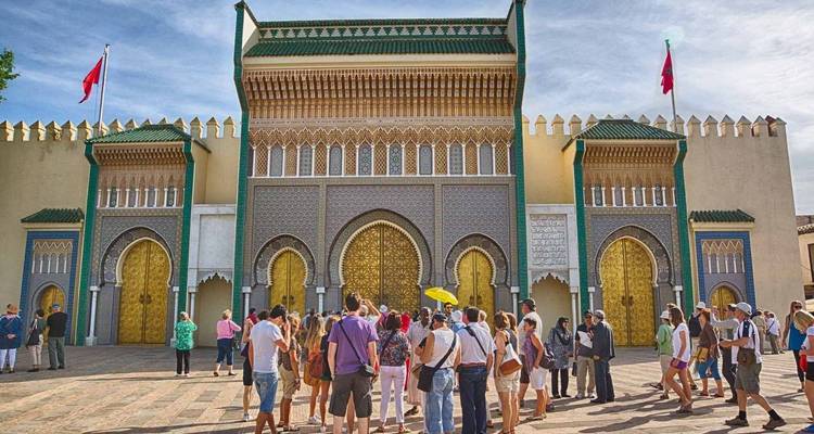 Group of tourists gathered outside a grand palace entrance.