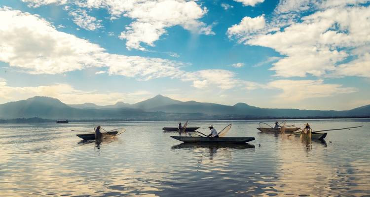 Traditional fishermen in canoes casting nets on the still waters of Lake Pátzcuaro with distant mountains.