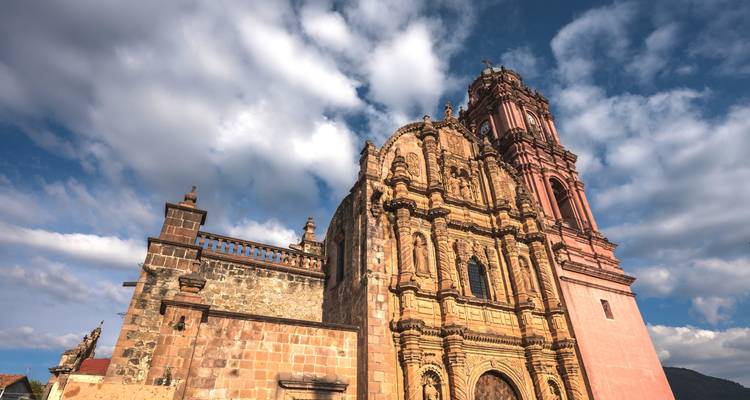 Baroque stone church facade with dramatic towers set against a sky of swirling clouds.