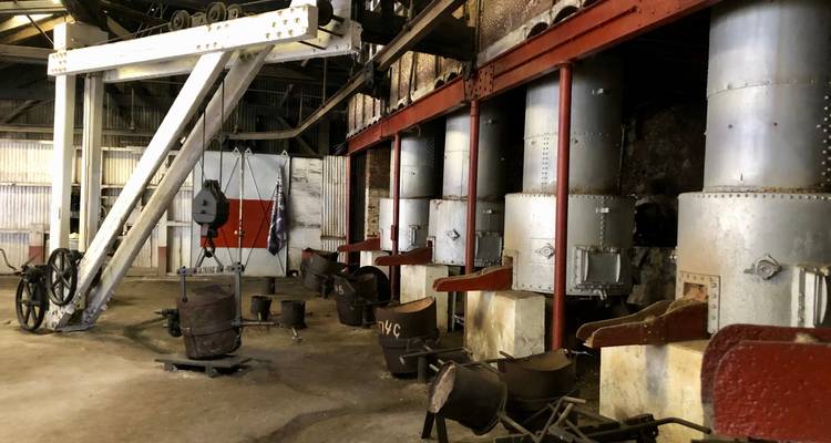 Interior of an old industrial distillery with large metal vats, pipes and machinery.