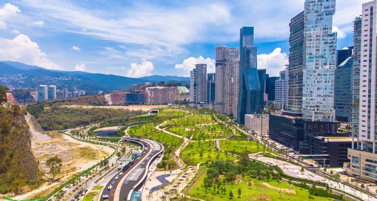 Modern skyline of Mexico City overlooking a lush linear park and winding elevated road on a bright summer day.