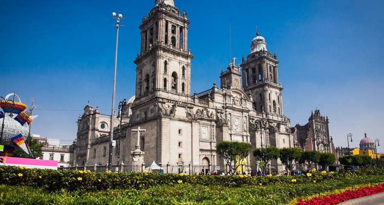 Close-up view of Mexico City Metropolitan Cathedral framed by vibrant flowerbeds under a clear blue sky.