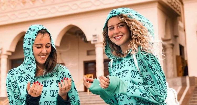 Twee vrouwen in bijpassende kleding die glimlachen voor een historische locatie.