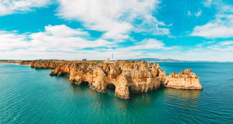 Vista de dron de impresionantes arcos marinos y acantilados a lo largo de la costa del Algarve bajo un cielo azul.
