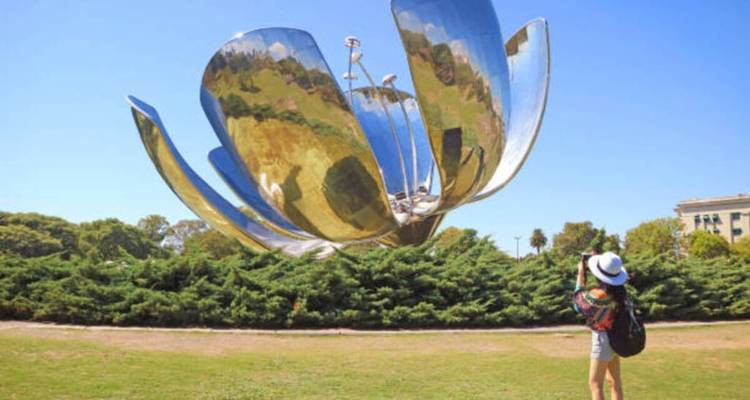 Une personne photographiant une grande sculpture de fleur métallique.