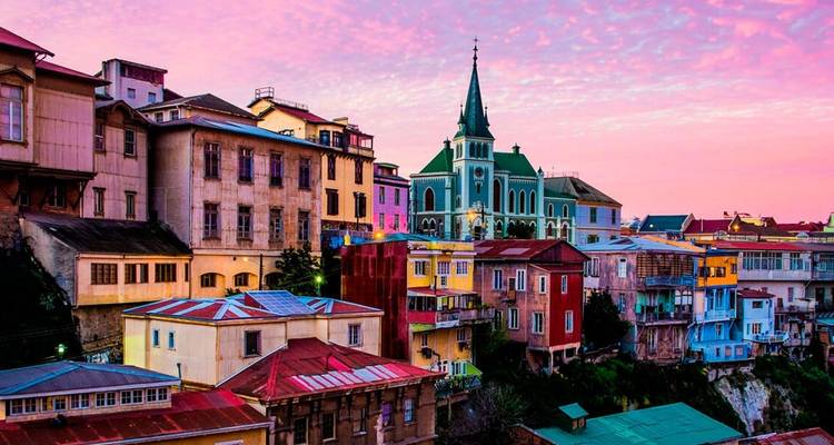 Bâtiments colorés à flanc de colline avec une église en arrière-plan au coucher du soleil.