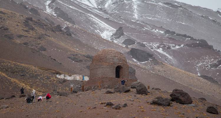 Una pequeña estructura de piedra en un paisaje montañoso con personas cerca.