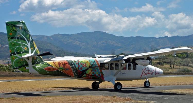 Pequeña aeronave colorida en una pista de aterrizaje con montañas al fondo.