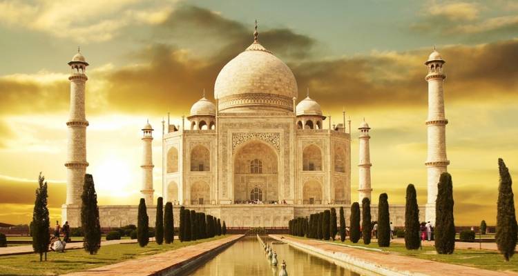Das ikonische Taj Mahal, getaucht in goldenes Sonnenuntergangslicht mit perfekter Spiegelung im langen zentralen Wasserbecken.