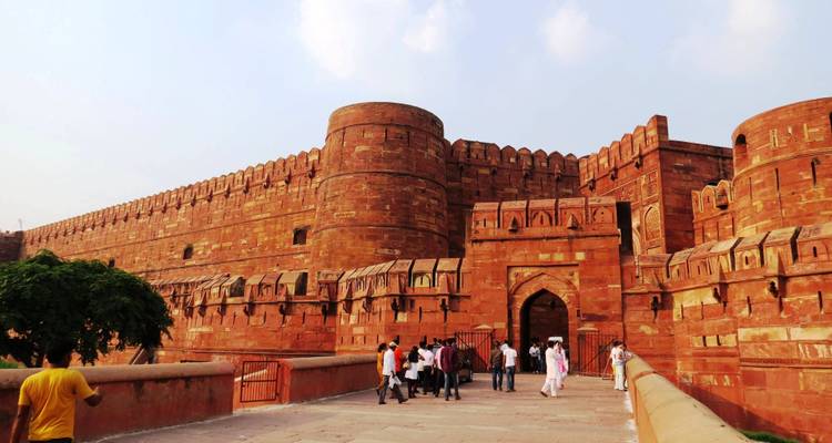 Massive rote Sandsteinmauern und Tor des Agra Fort mit eintretenden Touristen.