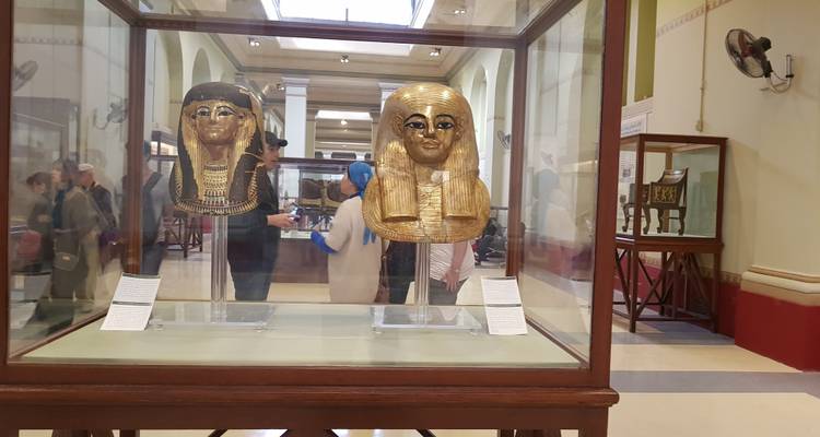 Máscaras de oro en exhibición en un museo con visitantes al fondo.