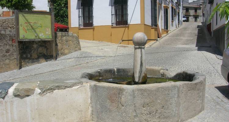 A stone fountain on a narrow street in a small town.