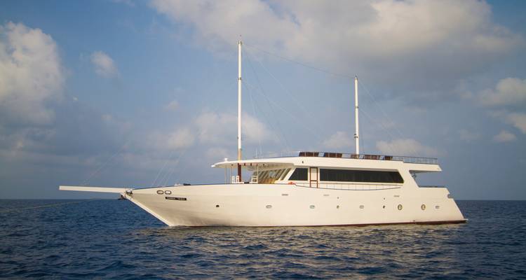 Élégant yacht blanc ancré sur les eaux bleues calmes de l'océan sous des nuages dispersés.