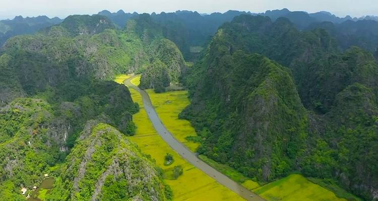 Aerial view of a river running between lush green mountains and rice fields.
