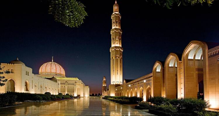 Vista nocturna de la Gran Mezquita del Sultán Qaboos iluminada con reflejos en el patio pulido