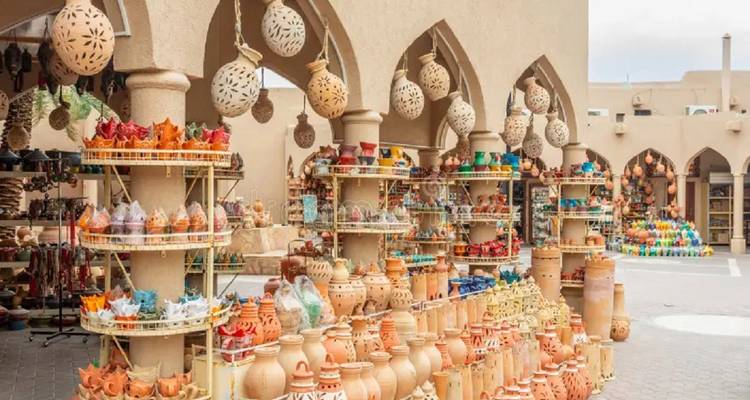 Des rangées de pots en argile colorés et de lanternes bordent les étagères d'un souk de poterie en plein air entouré de colonnades voûtées.