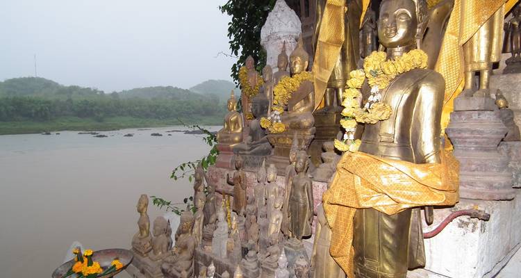 Statues of Buddhas adorned with yellow cloth and garlands overlooking a river.