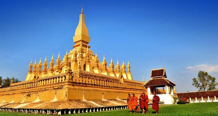 Monks walking past the golden Pha That Luang temple with a blue sky background.