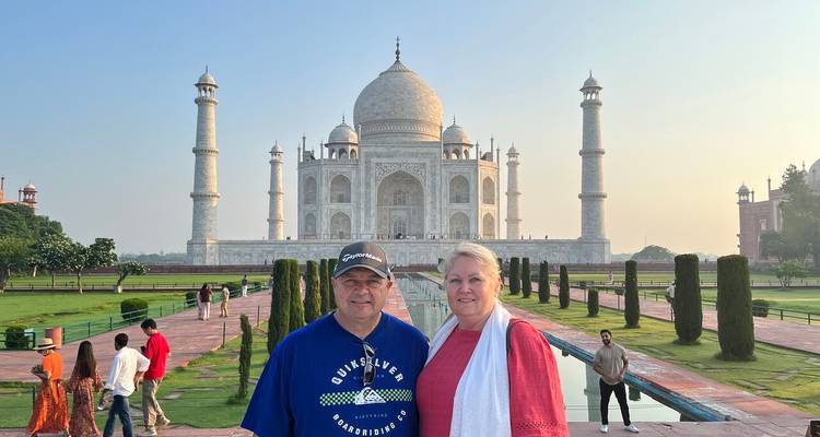 Smiling mature couple poses in front of the Taj Mahal on a clear morning.