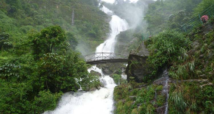 Malerischer Wasserfall mit einer darüber gespannten Brücke in üppiger Umgebung.