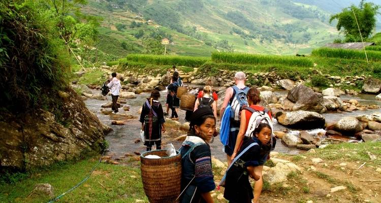 Menschen die een rotsachtige beek oversteken in een landelijk berggebied.