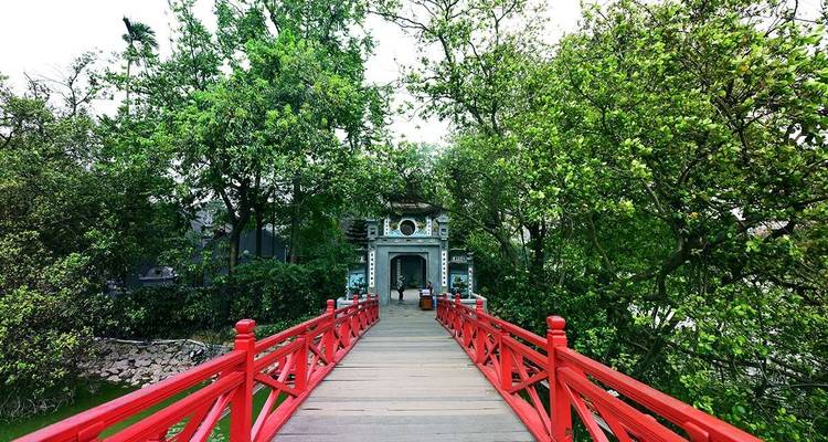 Rode brug die leidt naar een historische poort omgeven door weelderige groene bomen.