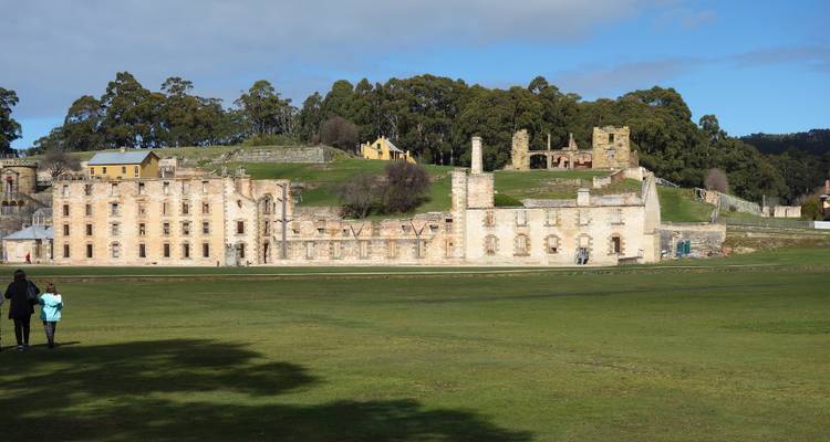 Au premier plan s'étend une vaste prairie menant aux ruines de grès du complexe pénitentiaire de Port Arthur sous un ciel nuageux parsemé.