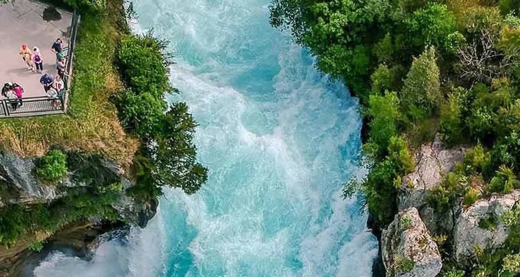 Rivière turquoise tumultueuse plongeant à travers une gorge étroite entourée d'une végétation luxuriante tandis que les visiteurs observent depuis un belvédère.