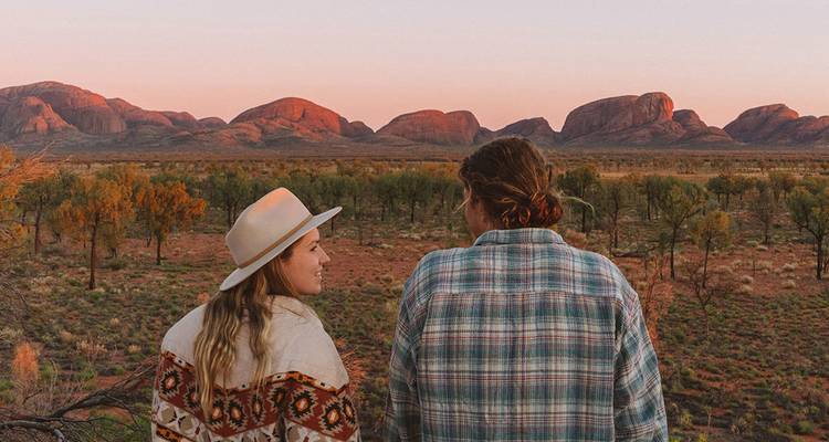Deux voyageurs regardent le coucher de soleil sur les dômes de Kata Tjuta dans le Centre rouge de l'Australie.